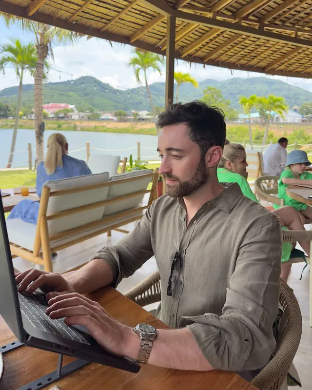 Patrick trabajando con su laptop en un café con vistas al lago en Phuket, Tailandia